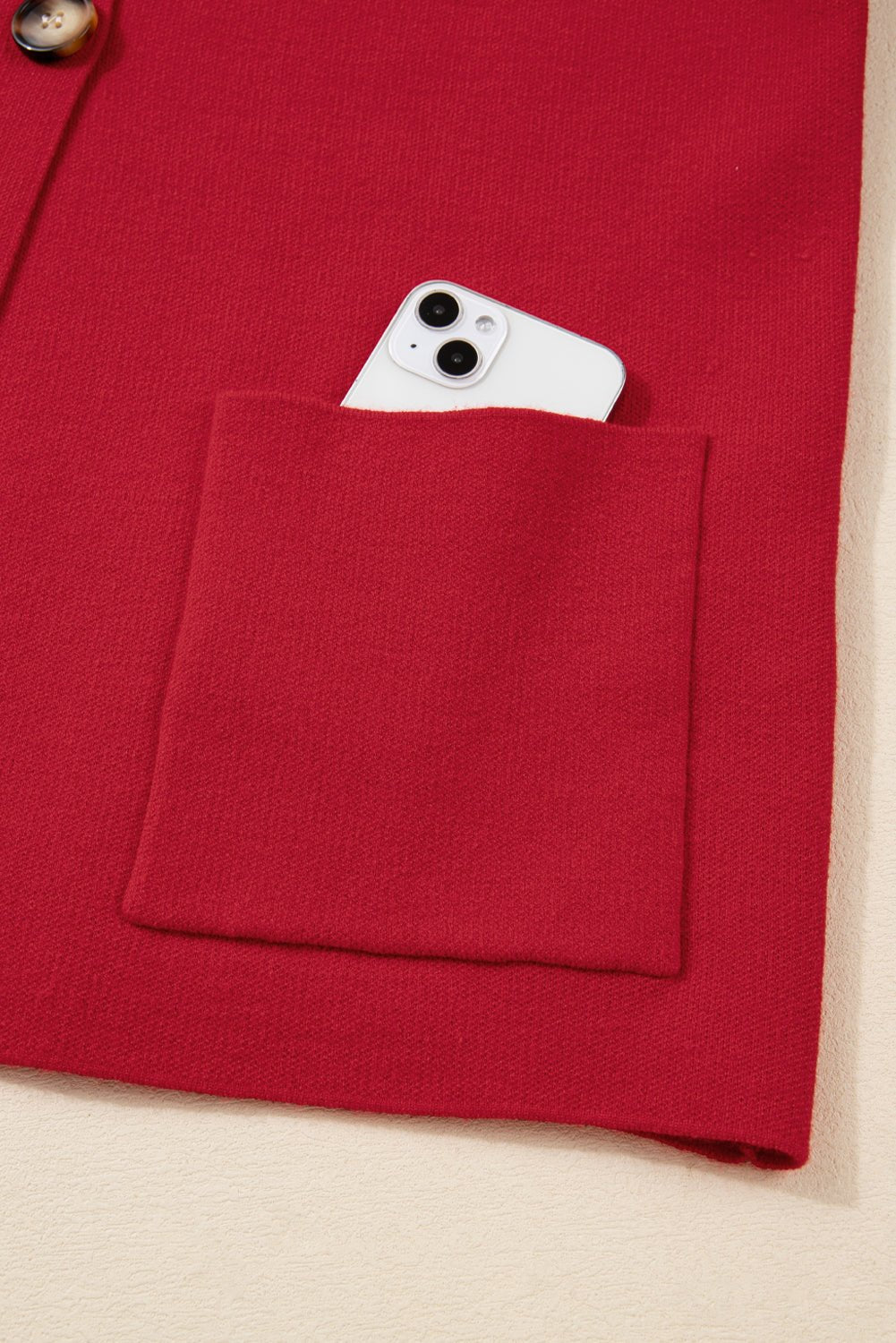Red jacket with a pocket containing a smartphone on a beige background