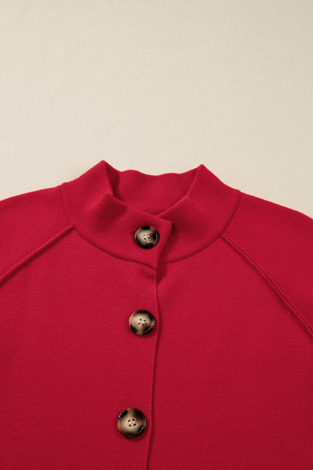 Close-up of a bright red knit mock-neck top with three dark brown metallic-detail buttons.