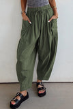 Person wearing green wide-leg pants and black sandals against a white wall.