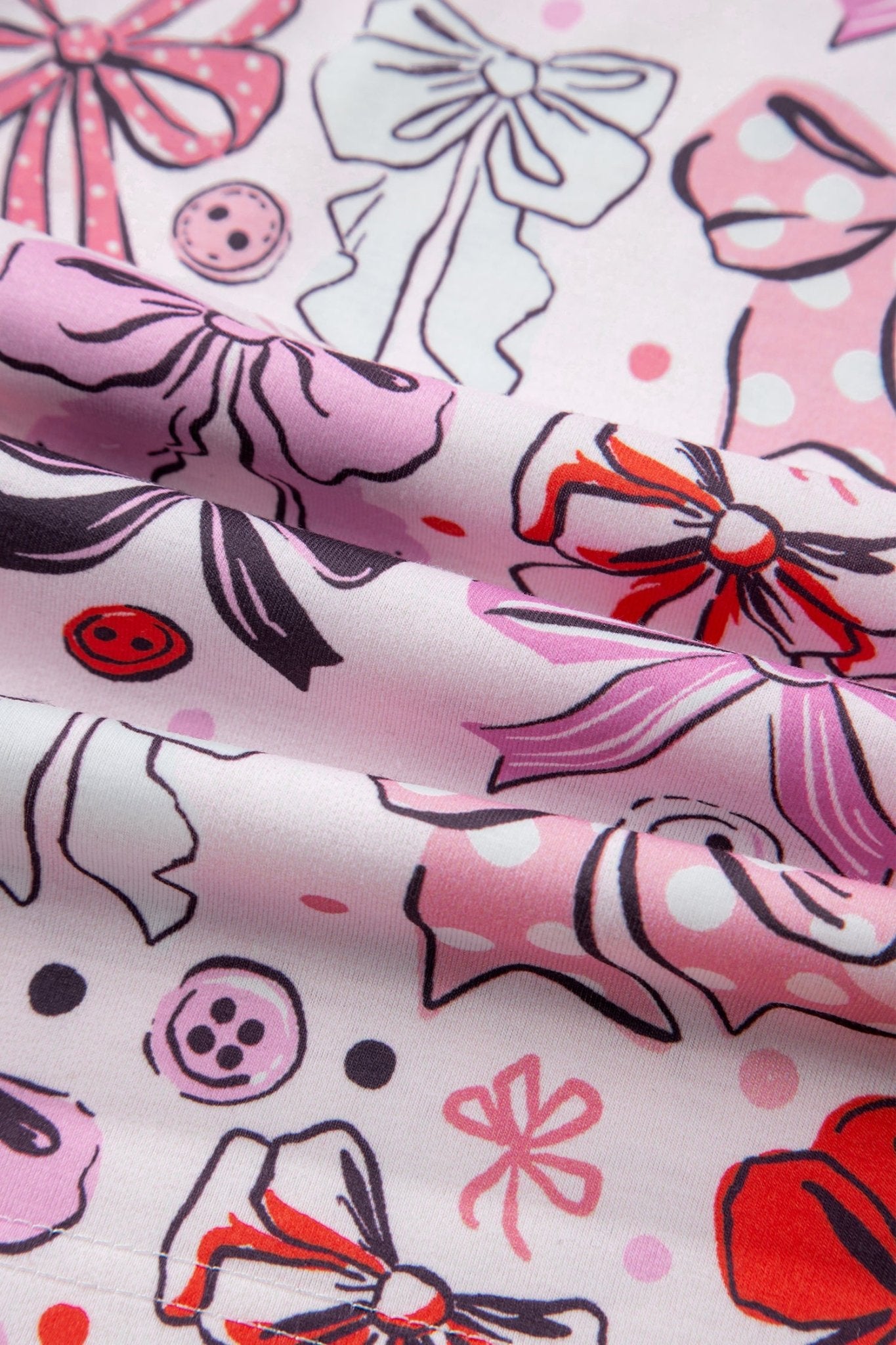 Fabric with pink bows, buttons, and polka dots on a white background