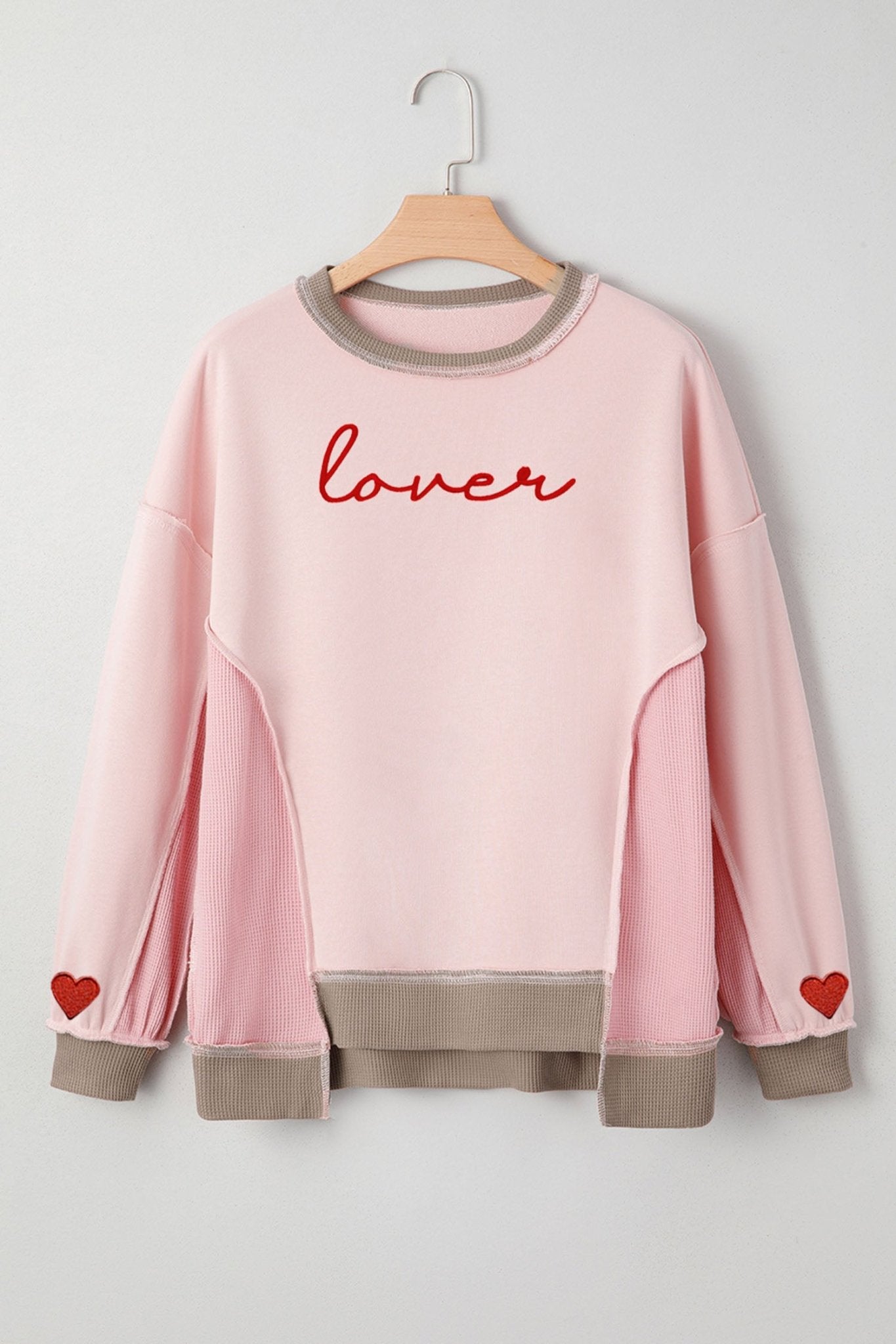 Pink sweatshirt with 'lover' text and heart designs on a hanger against a light gray background