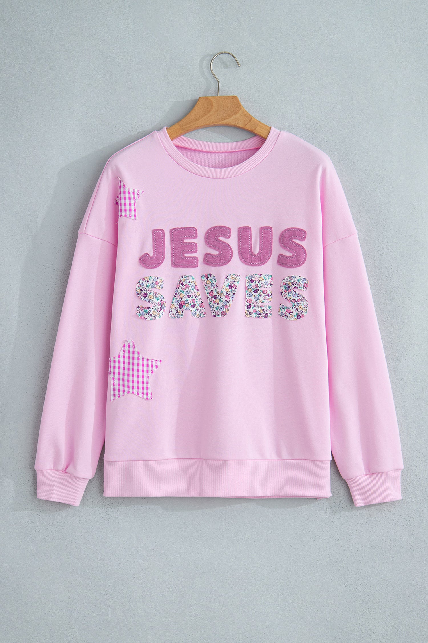 Pink JESUS SAVES faith sweatshirt with floral lettering and gingham star, flat lay