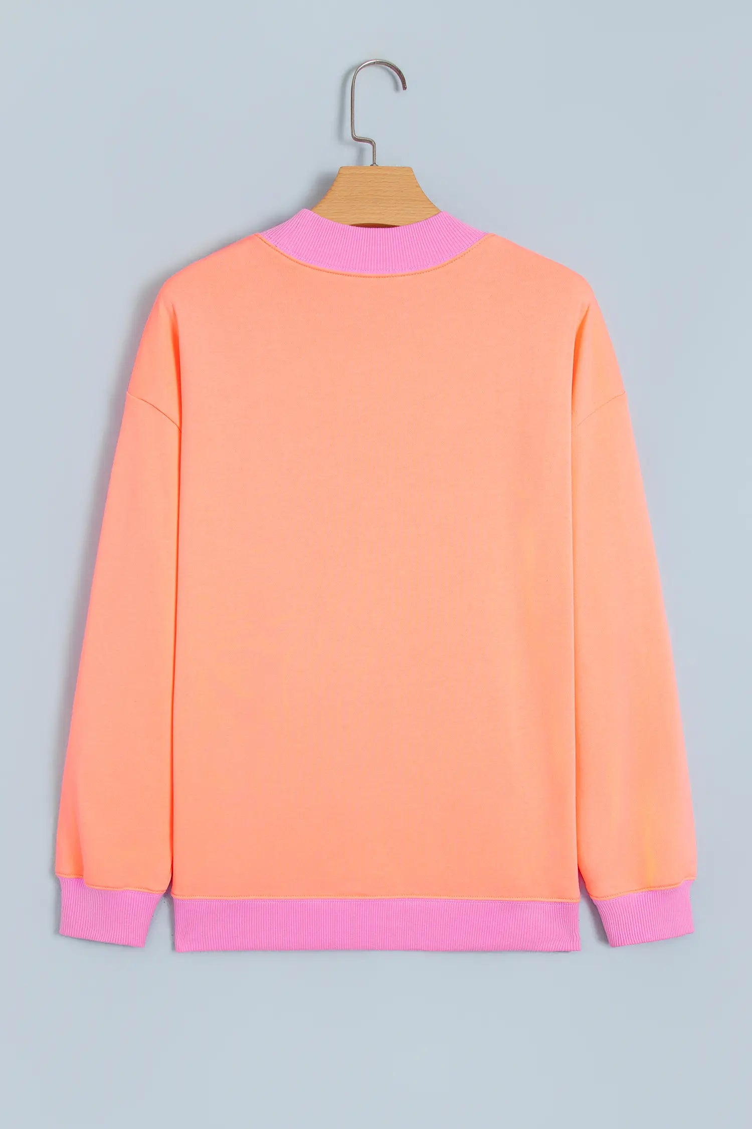 Orange sweatshirt with pink ribbed trim on a hanger, back view