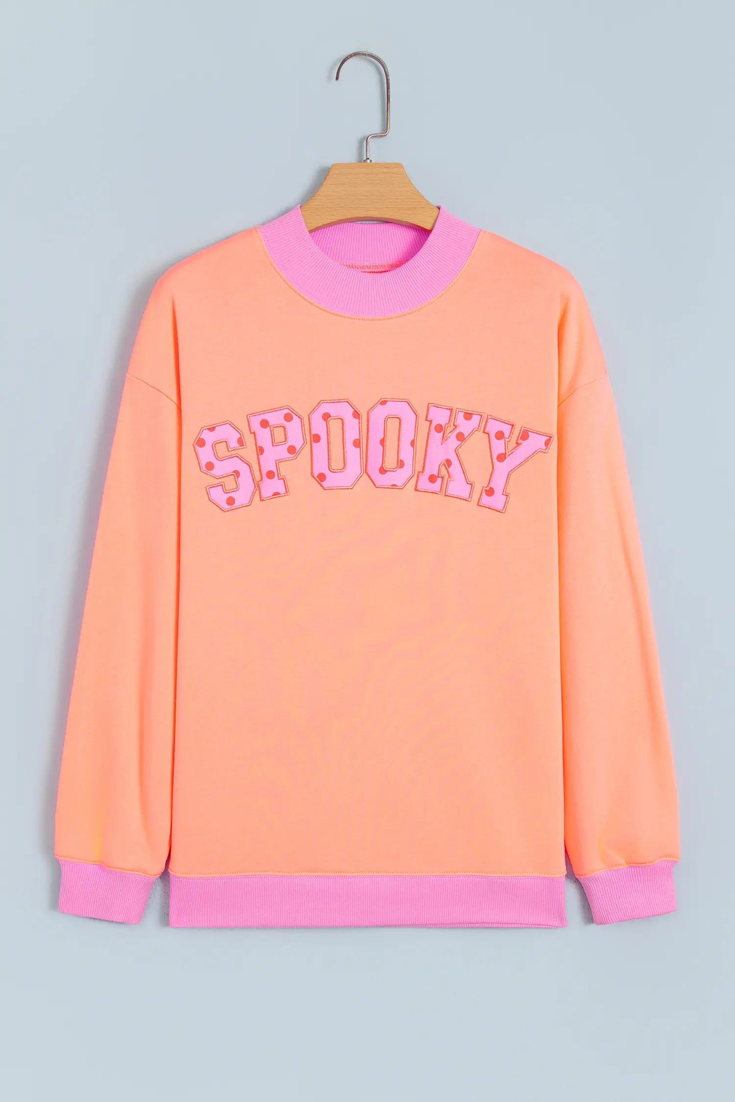 Orange SPOOKY slogan sweatshirt with pink trim on a hanger, front view