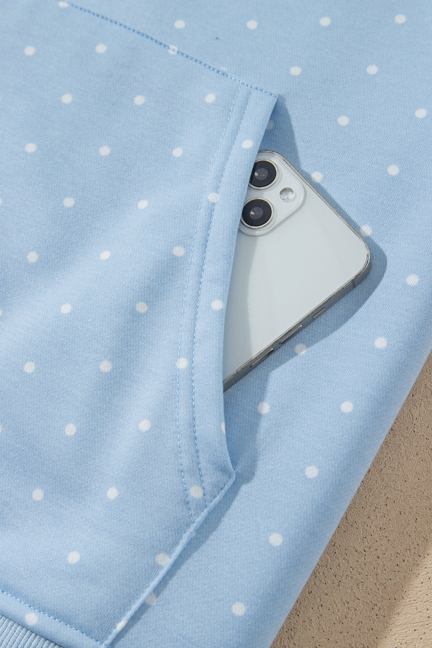 Sky blue polka dot hoodie kangaroo pocket holding a phone