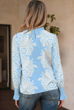 Person wearing a light blue floral blouse with long sleeves indoors.