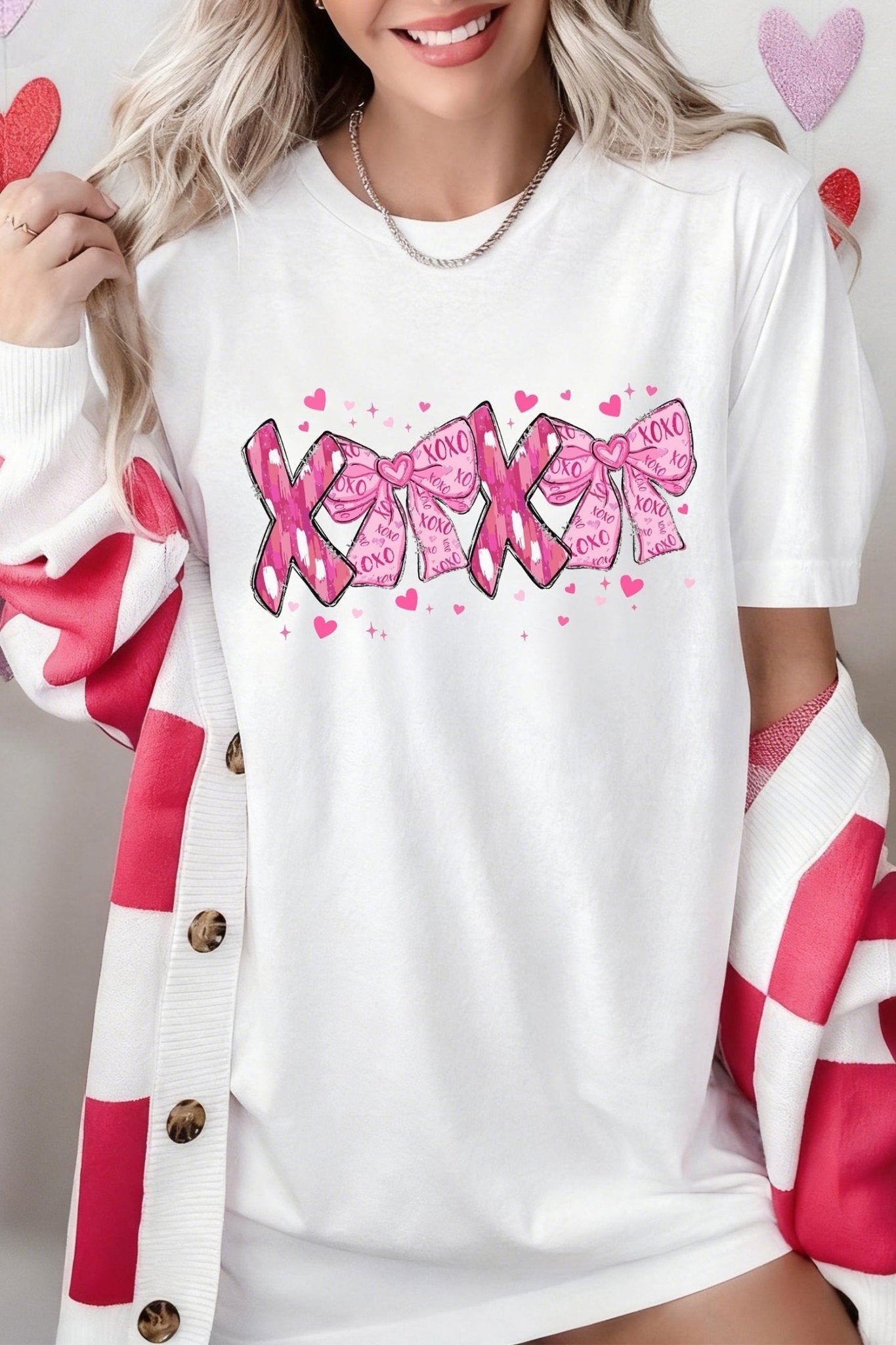 Person wearing a white shirt with pink text and hearts, holding a pink heart-shaped object.
