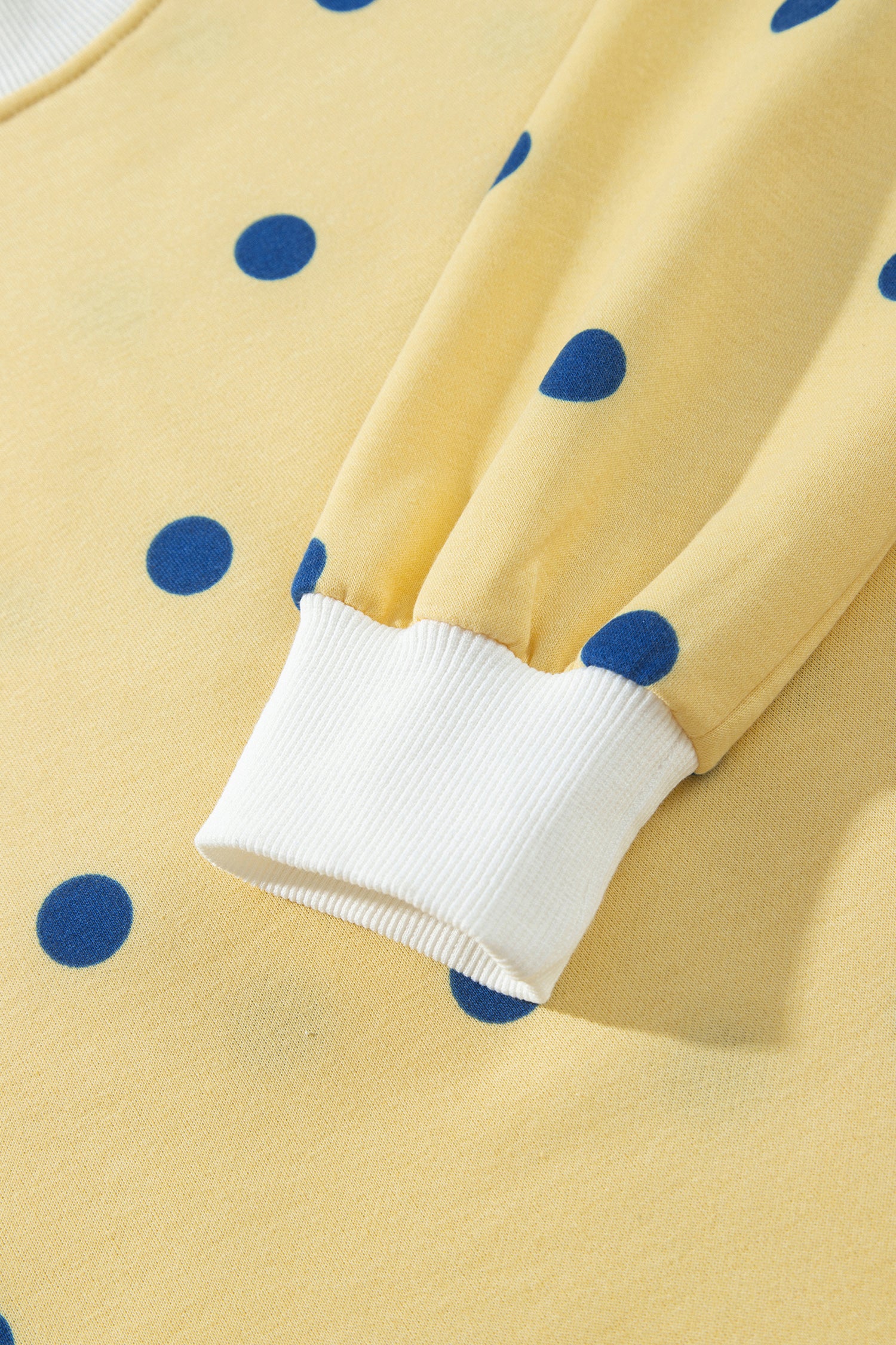 White ribbed sleeve cuff on yellow polka dot top, close-up