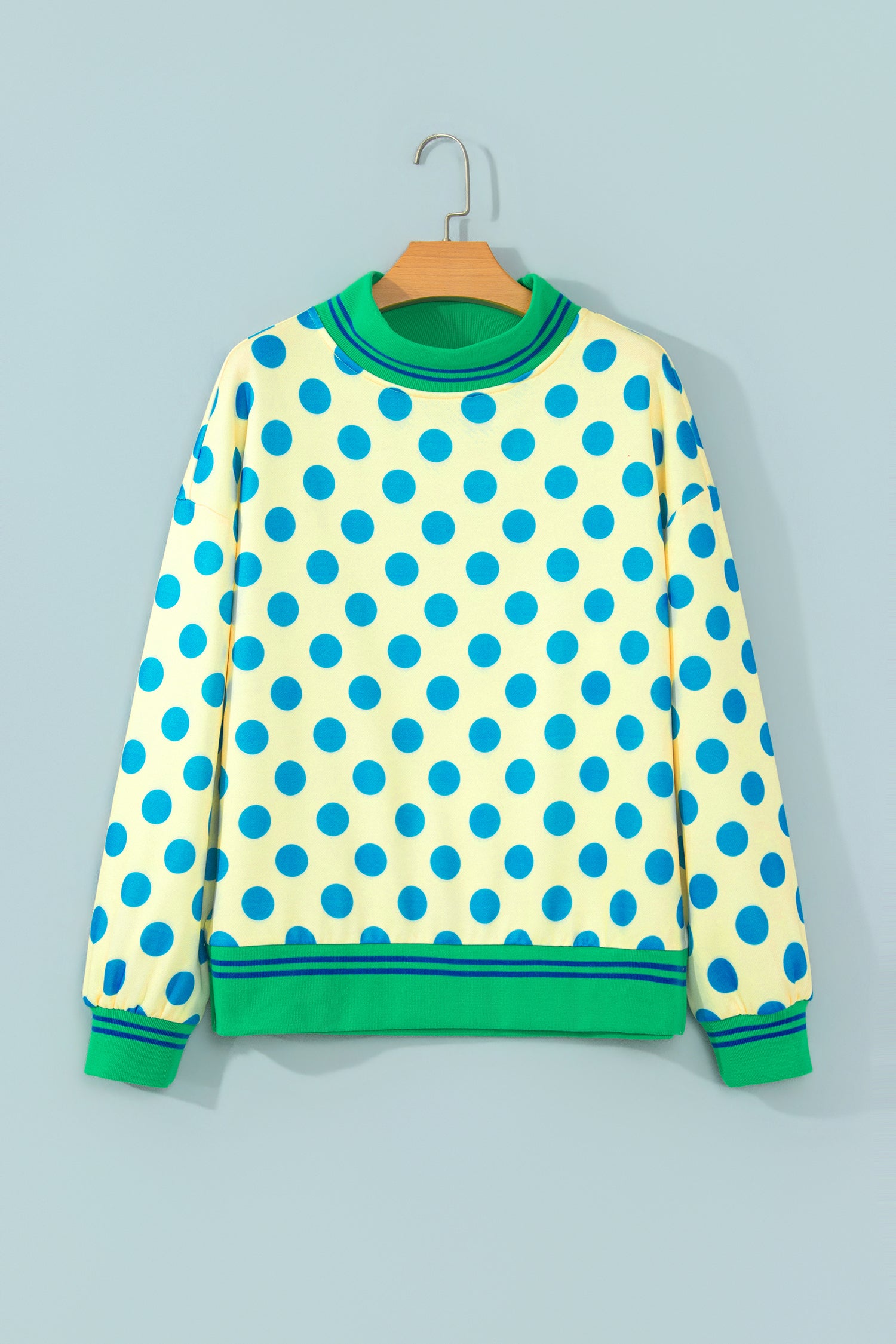 Yellow polka dot mock neck sweatshirt with green striped trim on a hanger