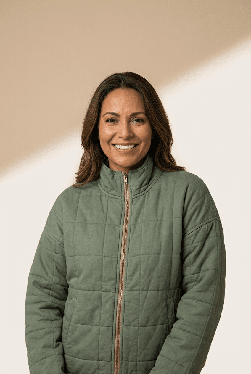 Smiling woman in an olive green quilted zip-up jacket against a warm beige background.