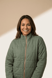 Smiling woman in an olive green quilted zip-up jacket against a warm beige background.
